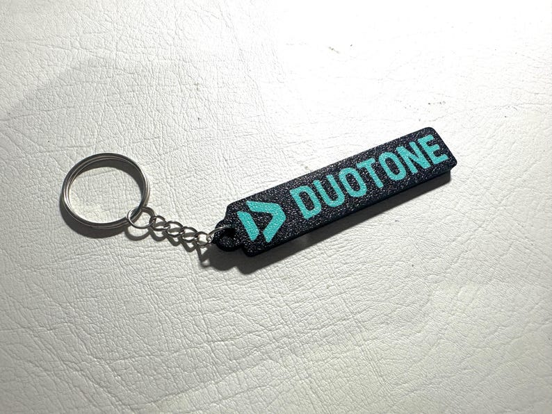 Peut inclure: Porte-cl&eacute;s noir avec un logo bleu turquoise et le mot "DUOTONE" imprim&eacute; dessus.