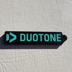 Peut inclure: Un porte-cl&eacute;s noir et turquoise avec le mot "DUOTONE" imprim&eacute; dessus.
