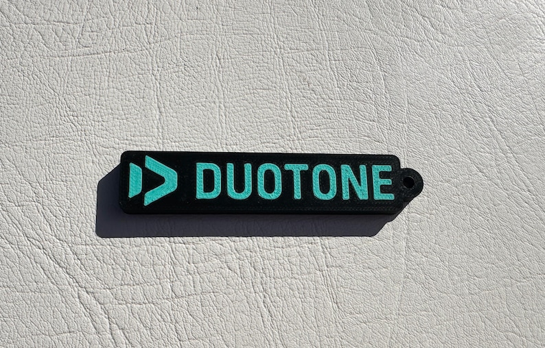 Peut inclure: Un porte-cl&eacute;s noir et turquoise avec le mot "DUOTONE" imprim&eacute; dessus.