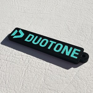 Peut inclure: Porte-cl&eacute;s noir avec un logo bleu turquoise qui dit "DUOTONE" avec une petite boucle &agrave; l'extr&eacute;mit&eacute;.