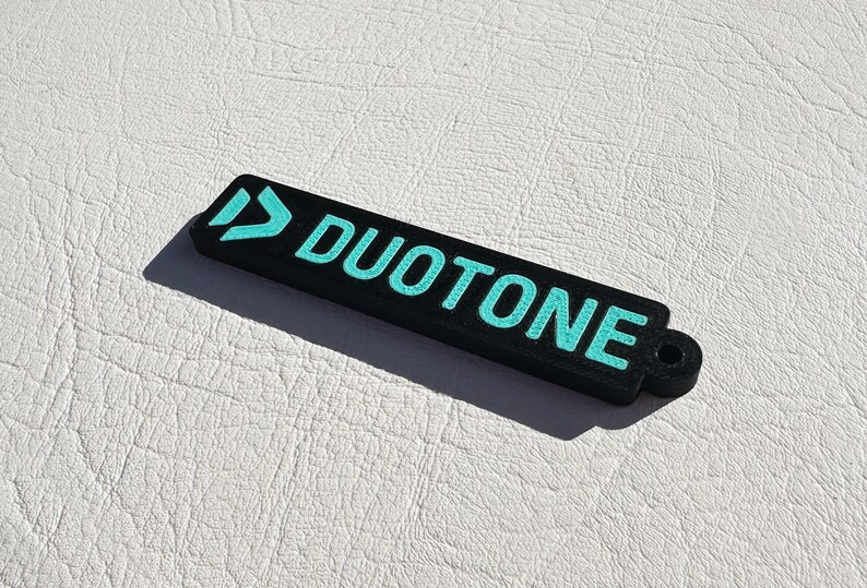 Peut inclure: Porte-cl&eacute;s noir avec un logo bleu turquoise qui dit "DUOTONE" avec une petite boucle &agrave; l'extr&eacute;mit&eacute;.