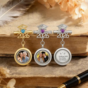 May include: Three graduation-themed pendants with the year 2026. One is gold-toned with a blue gem, the others are silver-toned with purple gems. Each has a photo pendant. One says "Walking With You Today and Always".