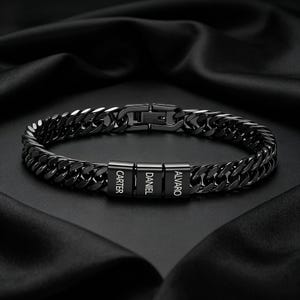 May include: Black chain bracelet with three rectangular name beads. The names "CARTER", "DANIEL", and "ALVARO" are engraved on the beads. The bracelet has a secure clasp and is displayed on a black satin surface.