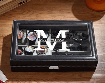 May include: Black leather watch box with a clear glass top. The box is divided into compartments holding watches, sunglasses, and a bracelet. The name "MATTHEW" is displayed in large white letters on the glass. The box is stitched with white thread.