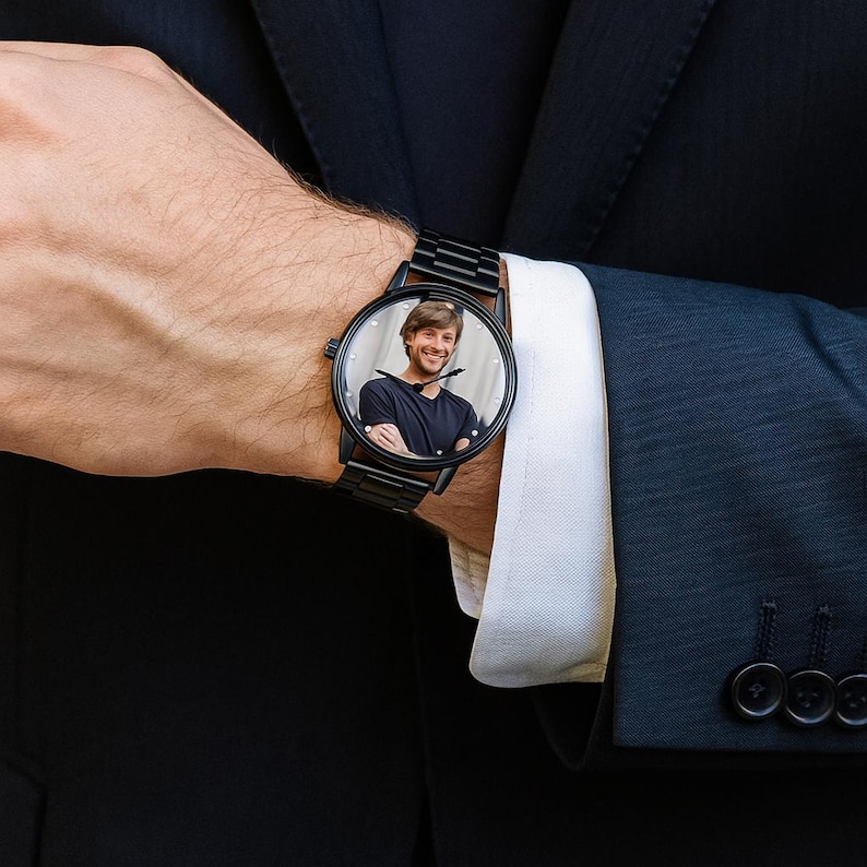 May include: A black wristwatch with a metal link band featuring a custom circular photo dial. The watch face displays a portrait of a smiling person wearing a dark t-shirt, with thin black hour and minute hands positioned over the image.