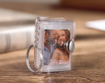 May include: A clear plastic keychain with a silver ring and a silver button. The keychain has a photo of a couple inside, with glitter embedded in the plastic.