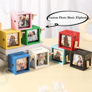 May include: A selection of multi-coloured, cube-shaped photo music flipbooks. Each cube is a different colour, including pink, yellow, green, blue, white, red, and black. The text "Forever Love" is printed on each cube. The text "Custom Photo Music Flipbook" is also visible.