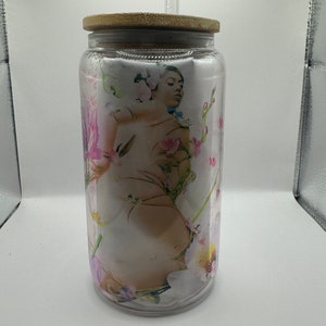 May include: A clear glass tumbler with a bamboo lid and a straw. The tumbler has a floral print with a woman's face in the center.