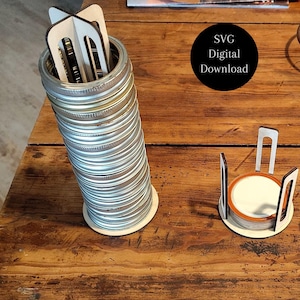 May include: A tall stack of silver metal mason jar rings held by a white laser-cut wooden stand, alongside a shorter stack of rings in a smaller white wooden stand. A black circular graphic with the white text SVG Digital Download is visible.