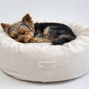 Small dog sleeping in organic cotton donut dog bed with natural raw cotton filling, soft supportive sides, and washable removable cover.