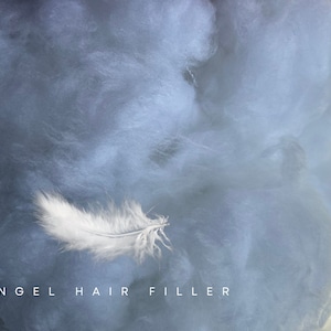 May include: A single white feather rests on a bed of fluffy white angel hair filler. The text "ANGEL HAIR FILLER" is printed below the feather.