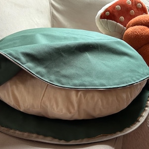 Round dog bed with a removable sage green cotton canvas cover partially unzipped to show the natural cotton insert.
