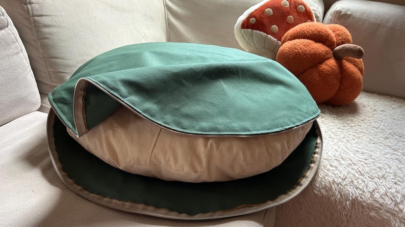 Round dog bed with a removable sage green cotton canvas cover partially unzipped to show the natural cotton insert.