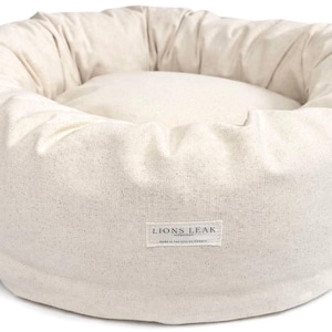 Organic cotton round dog bed in natural beige color with supportive raw cotton filling, removable washable cover, and minimalist donut design.