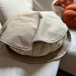 Round cotton canvas dog bed cover in tan color, displayed partially unzipped to show the cushion inside.