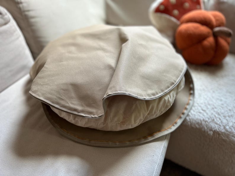 Round cotton canvas dog bed cover in tan color, displayed partially unzipped to show the cushion inside.