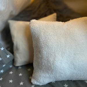 May include: Two white fluffy pillows with a soft, plush texture. The pillows are on a gray and white patterned surface.