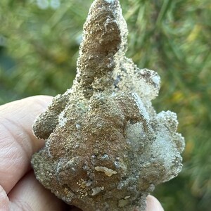 May include: A cluster of gray and brown crystals with a rough, textured surface. The crystals have a unique, organic shape and are reminiscent of a small mountain range.