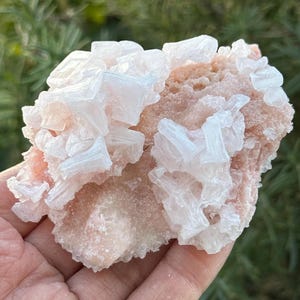 Peut inclure: Un amas de cristaux de sel rose de l'Himalaya avec une surface rugueuse et texturée. Les cristaux sont blancs et translucides, avec une structure délicate et en couches.