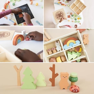 Pode incluir: Conjunto de brinquedos de madeira com um arco-&iacute;ris, &aacute;rvores, um urso, um cogumelo, um caracol e uma joaninha. O conjunto est&aacute; numa caixa de madeira com compartimentos. Os brinquedos s&atilde;o pintados em cores pastel.