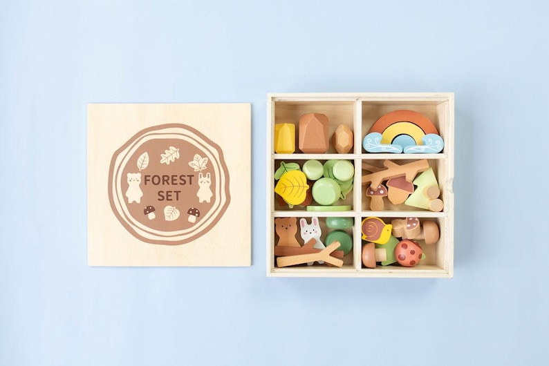 Pode incluir: Uma caixa de madeira cheia de pe&ccedil;as de madeira coloridas, incluindo animais, cogumelos, folhas e um arco-&iacute;ris. A caixa tem um r&oacute;tulo que diz "FOREST SET".