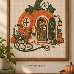 Puede incluir: Un patrón de punto de cruz enmarcado que muestra una gran casa de calabaza naranja con puerta y ventana verdes. Un perro se sienta dentro de la clínica de calabaza, que incluye estantes y un taburete. Un estetoscopio con diseño de huella enmarca la escena.