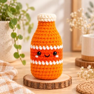 Peut inclure: Un jouet en crochet en forme de bouteille en fil orange vif avec un bouchon crème. Le corps présente deux rayures blanches en zigzag horizontales et un visage brodé amical avec des yeux en perles noires, un sourire et deux joues blanches.