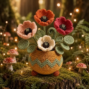 May include: A crochet flower arrangement featuring four poppies in shades of orange, pink, red, and white with dark centers. The flowers have green leaves and stems, and are displayed in a round, mustard-yellow pot with a green zigzag pattern.