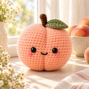 Puede incluir: Un juguete de peluche de ganchillo de color melocotón con forma de melocotón. Presenta un pequeño tallo marrón, una hoja verde, dos ojos de seguridad de plástico negro, una sonrisa negra bordada y dos pequeños círculos rosas en las mejillas.