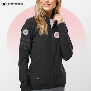 Może przedstawiać: Czarna kurtka zapinana na zamek z logo Adidas i trzema paskami na lewym rękawie. Kurtka ma dwa białe okrągłe logo z napisem "YOUR LOGO". Kurtka jest noszona przez osobę.