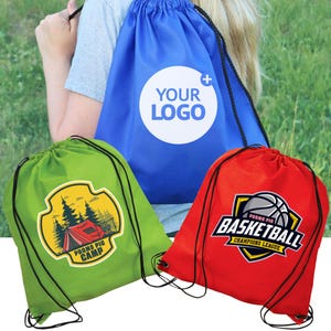 Pode incluir: Três sacos com cordão em azul, verde e vermelho. O saco azul tem um círculo branco com o texto "YOUR LOGO". O saco verde apresenta uma cena de acampamento com o texto "PROMO PIG CAMP". O saco vermelho exibe um gráfico de basquete com "BASKETBALL CHAMPIONS LEAGUE".