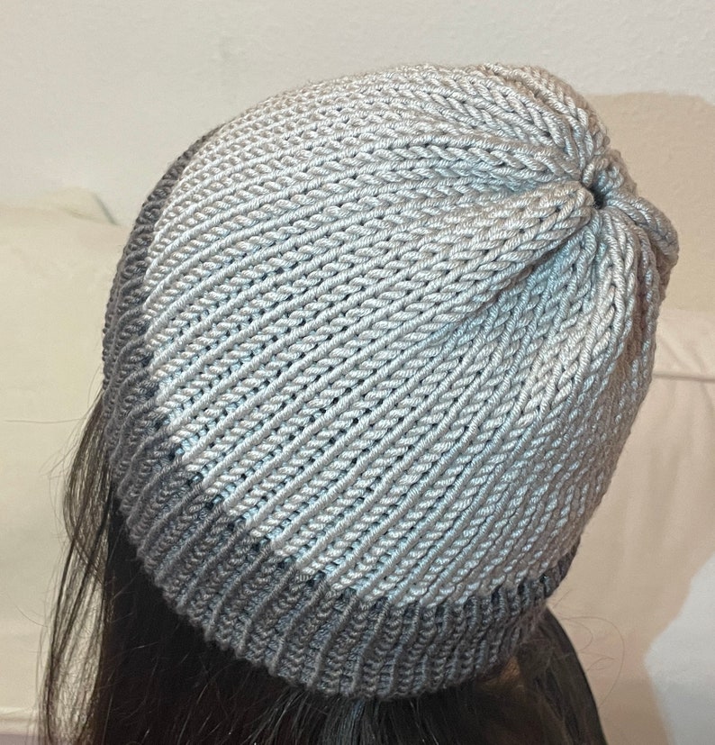 K&ouml;nnte beinhalten: Eine graue und wei&szlig;e Strickm&uuml;tze mit Rippenstruktur. Die M&uuml;tze hat einen dunkelgrauen Band am unteren Rand.