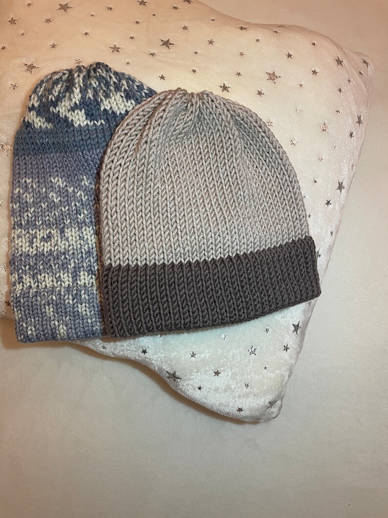 K&ouml;nnte beinhalten: Zwei Strickm&uuml;tzen, eine graue mit braunem Rand und eine blau-wei&szlig; gemusterte M&uuml;tze.