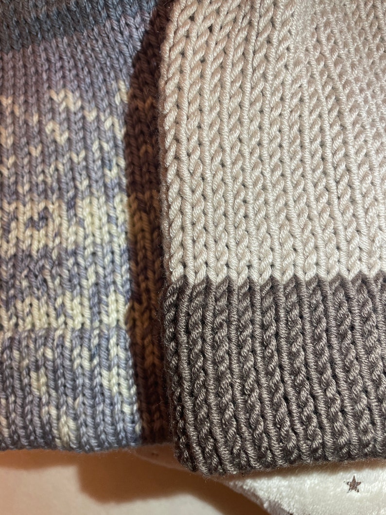 K&ouml;nnte beinhalten: Zwei Strickm&uuml;tzen, eine mit einem grau-wei&szlig;en Ombre-Muster und die andere mit einem beige-braunen Farbblockmuster.