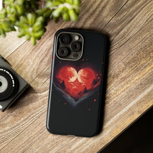 May include: A black phone case with a red heart design. The heart is made up of two red moons with a forest scene inside. The phone case has a camera lens cutout.