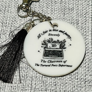May include: White round keychain with a black and white illustration of a typewriter and the text "All's fair in love and poetry... Sincerely TIP The Chairman of The Tortured Poets Department".