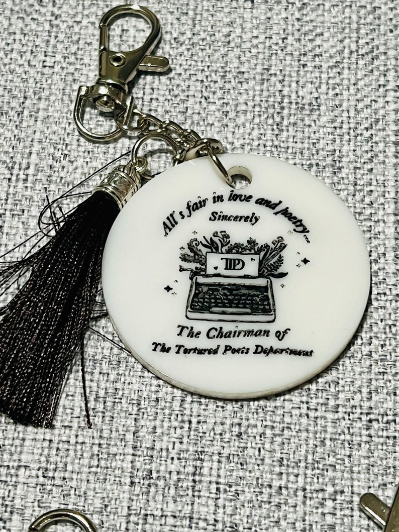 May include: White round keychain with a black and white illustration of a typewriter and the text "All's fair in love and poetry... Sincerely TIP The Chairman of The Tortured Poets Department".