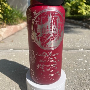 May include: A red stainless steel water bottle with a black lid and a silver engraved design of Hogwarts castle and the quote "I solemnly swear that I am up to no good."