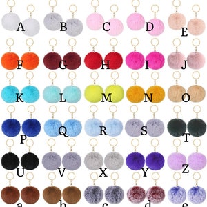 May include: Assortment of 26 colorful fluffy pom pom keychains with gold key rings. The pom poms are arranged in alphabetical order from A to E, F to J, K to O, P to T, U to Z, and a to e.
