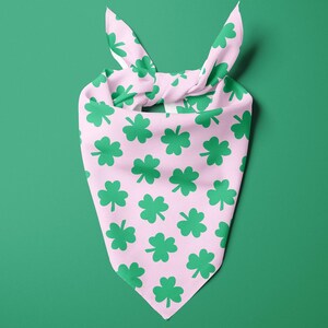 May include: A pink bandana with a green shamrock pattern. The bandana is tied at the top, with the ends forming a knot. The background is a solid green color.
