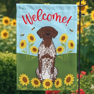 May include: A welcome garden flag with a brown and white German Shorthaired Pointer dog sitting in a field of sunflowers. The flag is blue with the word "Welcome!" in red letters.