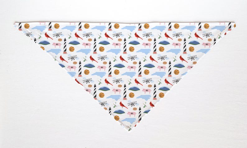 May include: White triangular bandana with a repeating pattern of North Carolina state symbols. The design includes red cardinals, basketballs, airplanes, pigs, lighthouses, and the state outline.
