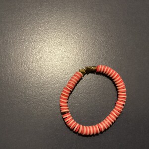 May include: A pink and white striped bracelet with gold star accents.