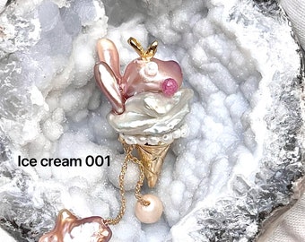 May include: A pink and white pearl ice cream cone pendant with a gold chain and a pink pearl charm. The pendant is displayed in a white geode.