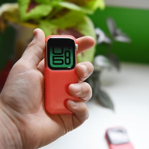 May include: A red silicone case for an Apple Watch with a black digital clock face displaying the time 0:58.