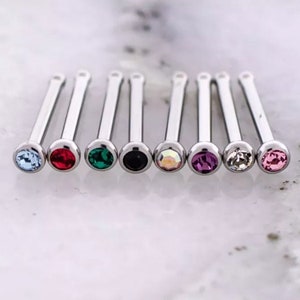 May include: Eight silver nose rings with different colored gems. The gems are blue, red, green, black, iridescent, purple, clear, and pink.