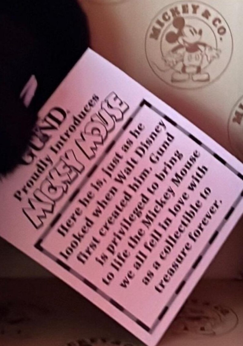 May include: A pink tag with black text introduces "Mickey Mouse" by Gund. The tag includes text about the character's creation and the brand's privilege in bringing Mickey Mouse to life as a collectible.