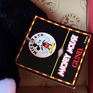 May include: A black tag with red and yellow trim features the text "Mickey Mouse Gund Antique" and a Mickey Mouse graphic. The tag is attached to a black and white plush toy.