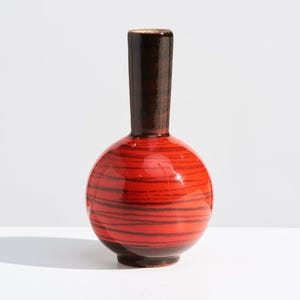 May include: A small, round ceramic vase with a red and black striped pattern. The vase has a dark brown neck and base. The vase is approximately 6 inches tall.