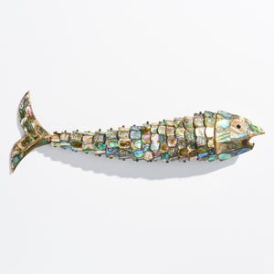 May include: A silver fish-shaped bottle opener with a mother-of-pearl inlay. The fish has a detailed tail and scales.